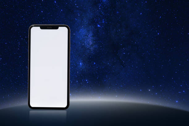 A phone is on a table in front of a starry sky. The phone is white and black