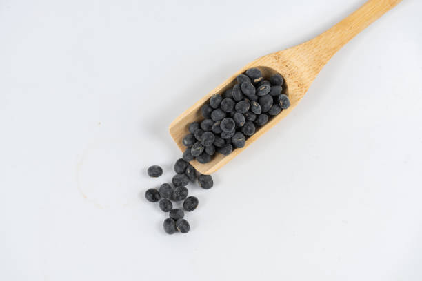 Black beans in wooden spoon and scattered on white background