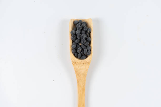 Black beans in wooden spoon and scattered on white background