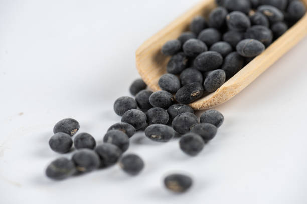 Black beans in wooden spoon and scattered on white background