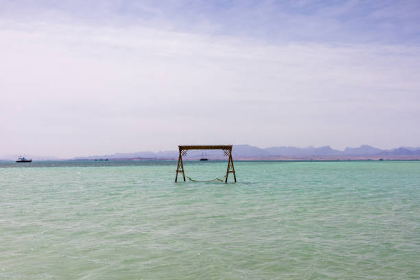 A serene seascape featuring a hammock suspended over crystal-clear waters, set against a backdrop of distant mountains and a tranquil shoreline. the turquoise hues and cloud-dotted sky enhance the peaceful ambiance, making it ideal for promoting relaxation and travel. perfect for themes of escape and leisure, capturing the essence of a coastal getaway.