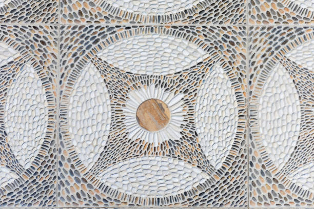 A close-up view of a geometric stone mosaic pattern featuring intricate pebble detailing. the design displays symmetry with circular motifs, using a natural palette of beige, brown, and white. ideal for interior or exterior decorative purposes, this pattern essence of organic, earthy elegance. perfect for architectural projects or artistic endeavors.