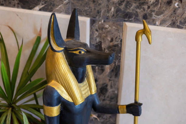 Intricate depiction of the ancient egyptian deity anubis adorned with gold highlights, set against a refined marble backdrop. the statue's black surface contrasts elegantly with the gold details and ceremonial staff, embodying the mystique of egyptian mythology. ideal for exhibits, educational materials, and cultural discussions.