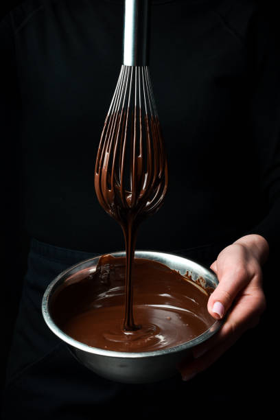 istock A bowl of melted chocolate and a kitchen whisk are held by hands. Kitchen utensils. On a black background. 2190898478
