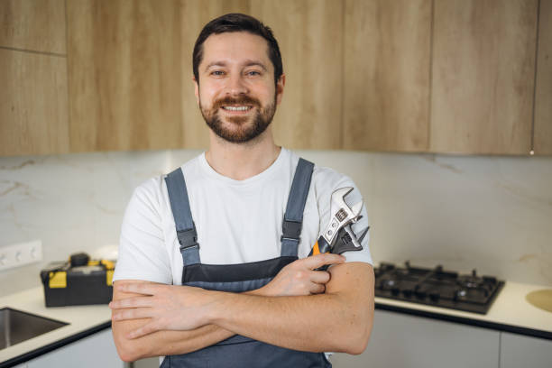 istock smiling handsome plumber standing with crossed arms and looking at camera in kitchen holding wrench and tools 2190903080