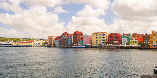 Willemstad, Curacao, Netherlands - January 6, 2018: A row of brightly colored colonial buildings lining the waterfront in Willemstad, Curacao, with their reflections shimmering in the calm harbor waters.