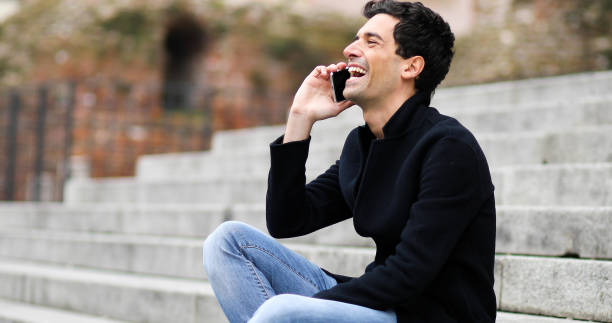 istock Young man laughing while talking on mobile phone on stairs 2190907695