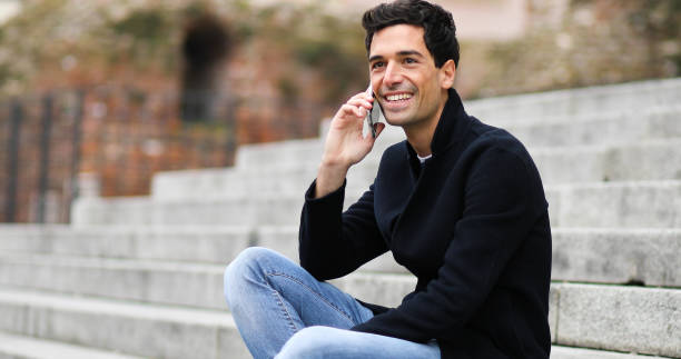 istock Young man smiling while talking on mobile phone on stairs 2190907709