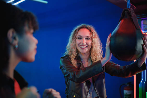 istock Young woman playing punching arcade game with friend 2190911226