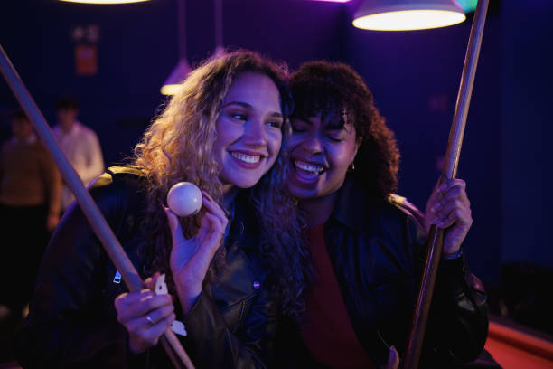 Young smiling cheerful two young women are playing billiards in bar after work. They are involved in recreational activity.