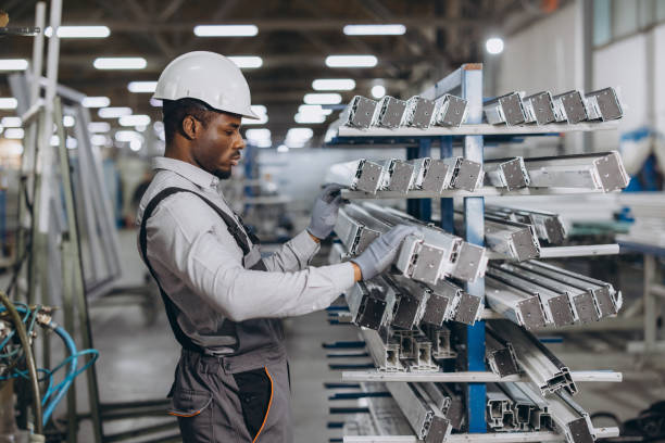 Concentrated african american factory worker wearing safety helmet selecting aluminum profiles for windows and doors production in workshop