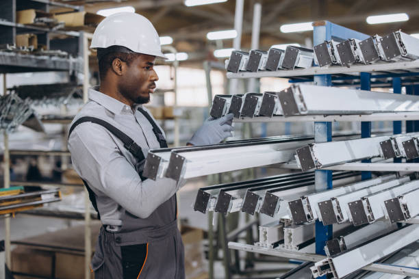 African american factory worker wearing hardhat and gloves checking aluminum and pvc window and door frames in production line