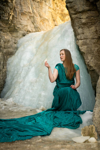 cute blonde girl in fairy costume with wings. girl sitting on pier near river. fairy wings white, made of transparent chiffon, decorated with pearls. concept of magic and nature. top view. looking at camera
