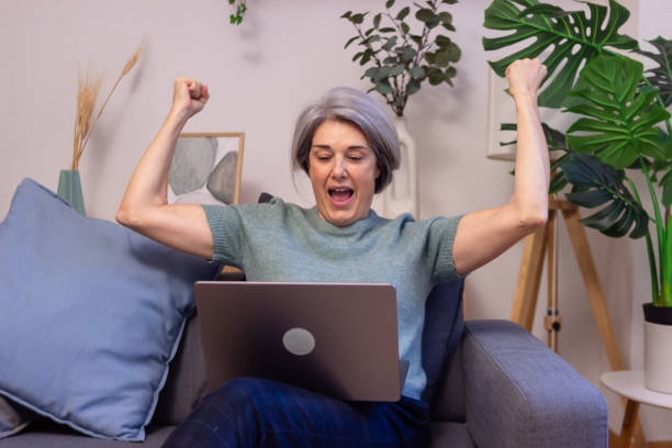 istock Excited mature woman celebrating success while using laptop at home 2190939479