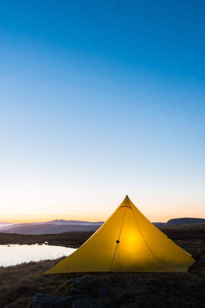 istock Yellow tent wild camping beside mountain lake at sunrise copyspace 2190942268