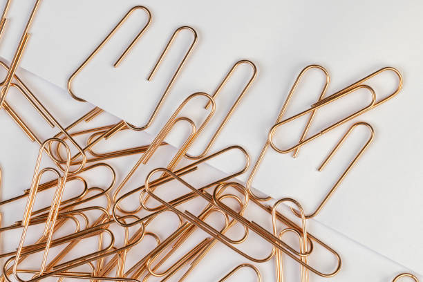 An abundance of silver paper clips on a wooden surface with one colored paperclip in amongst the uniform silver ones.