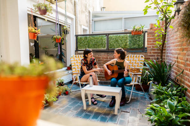 Female friends talking and playing guitar in the backyard