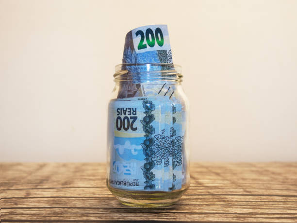 istock Brazilian real notes in transparent glass jar bottle container placed put isolated on table with white background. savings concept 2190955595