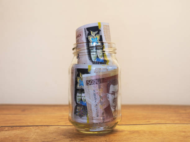 istock Jamaican dollar notes in transparent glass jar bottle container placed put isolated on table with white background. savings concept 2190955704