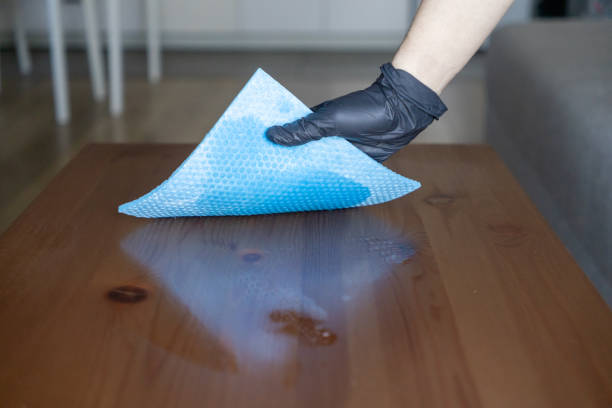istock cleaning a wooden table with a blue microfiber cloth and spray, gloved hand ensuring a polished and hygienic surface 2190956276