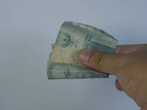 istock Hand holding a 2,000 rupiah note against a white background 2190956335