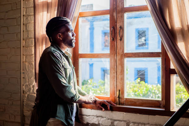 istock Young man contemplating while looking through the window at home 2190962970