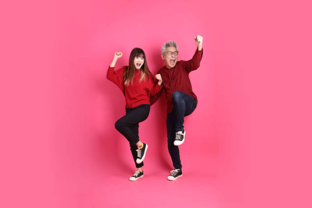 Chinese New Year, Asian senior man and woman wear santa hat, casual red clothes with gesture of yes, excited, celebrating, isolated on pink background.