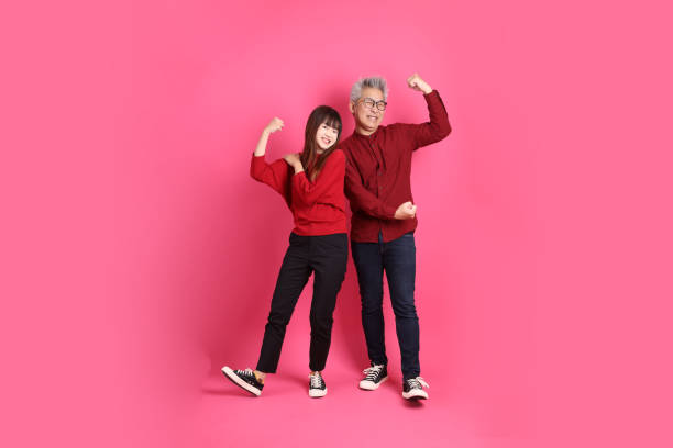 Chinese New Year, Asian senior man and woman wear santa hat, casual red clothes with gesture of healthy, strong, isolated on pink background.