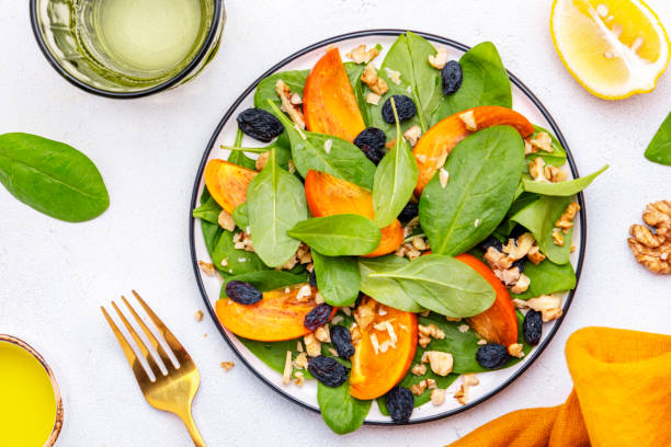istock Wintervegan persimmon salad with walnuts, blue raisin and spinach, white background, top view 2190973811