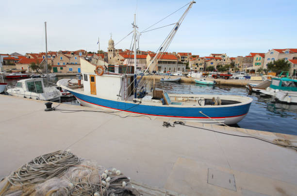 Bright red fishing trawler vessel moored at a quiet harbor in Istria, Croatia, with a large net suspended from a crane under a partly cloudy sky, capturing the essence of coastal marine life.