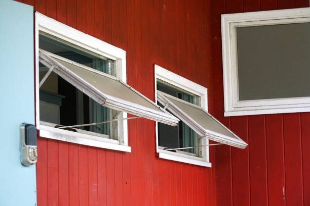 Solid red, two-story New England barn viewed from a corner with windows and red shutters opened at various angles. Shiplap construction.
