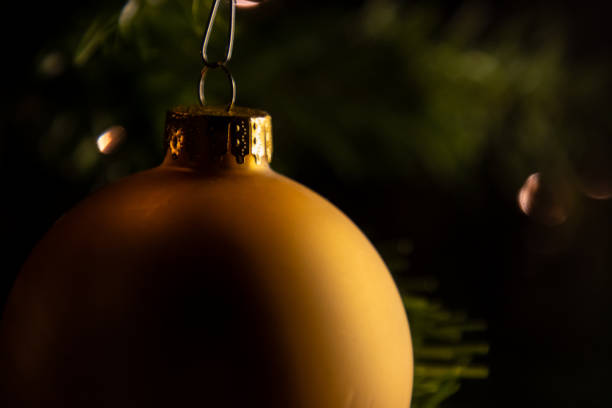 Close-up of golden Christmas baubles scattered against a sparkling bokeh background. The soft focus on the lights creates a warm, festive atmosphere, perfect for holiday-themed projects, greeting cards, and Christmas decorations.