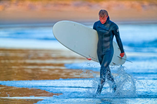 The Pacific Rim National Park in British Columbia on March 02, 2024: Young male surfer returning after a session at Pacific Rim National Park on Vancouver Island at sunset, British Columbia