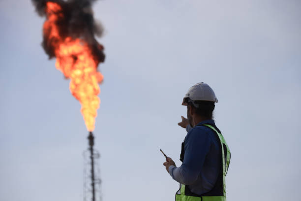 istock A senior engineer is using a walkie-talkie while standing against the background of a fire blazing from a factory. 2191007660