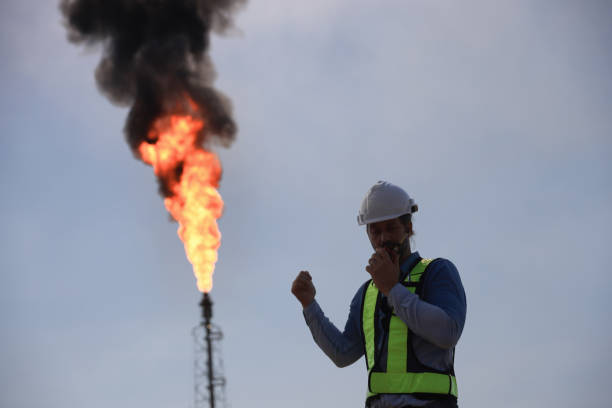 istock A senior engineer is using a walkie-talkie while standing against the background of a fire blazing from a factory. 2191007662