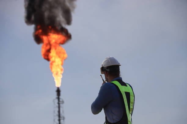 istock A senior engineer is using a walkie-talkie while standing against the background of a fire blazing from a factory. 2191007663