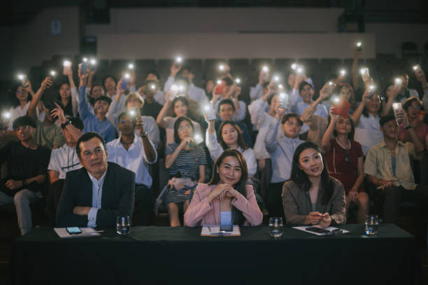 istock Asian panel judges giving score to stage performance competition in front of audience with fans waving smartphone led lights supporting at the back 2191026701