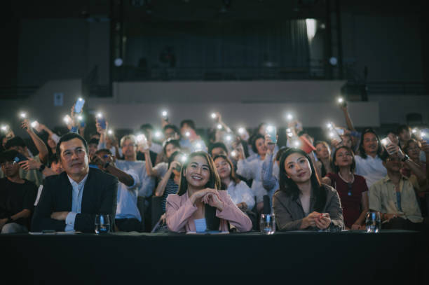 istock Asian panel judges giving score to stage performance competition in front of audience with fans waving smartphone led lights supporting at the back 2191026727