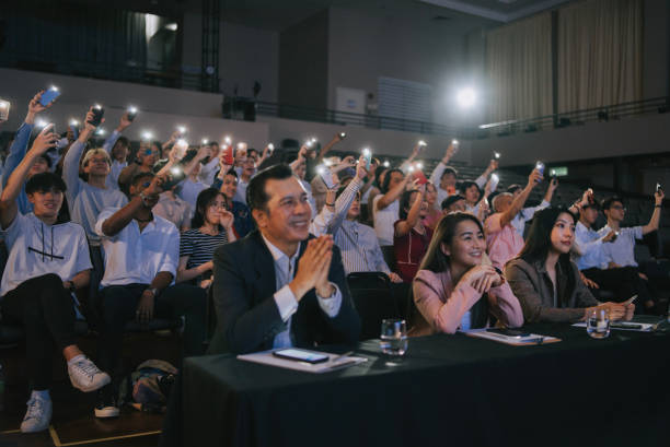 istock Asian panel judges giving score to stage performance competition in front of audience with fans waving smartphone led lights supporting at the back 2191026998