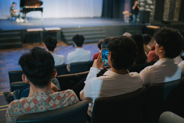 istock rear view Asian man texting message with smartphone in classical concert 2191027119