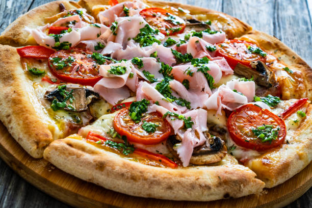 istock Pizza with ham, mozzarella cheese, sliced tomatoes and white mushrooms on wooden table 2191030075