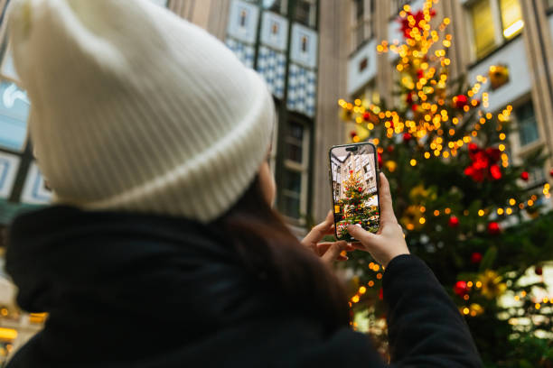 A young woman takes photos of a beautifully decorated Christmas tree at Berlin's Christmas market. The glowing holiday lights create a magical atmosphere