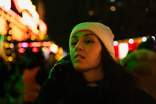 A young woman, illuminated by the vibrant holiday lights, speaks on her phone while enjoying the atmosphere of the Berlin Christmas market. Her white beanie and black gloves highlight her winter style amidst the golden bokeh of Christmas decorations in the background