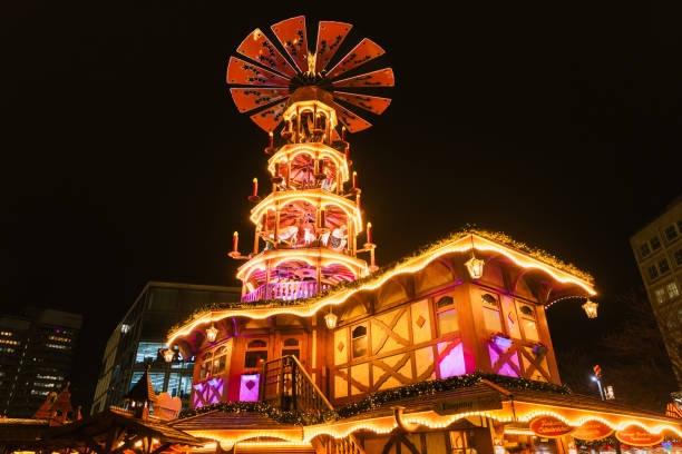 A beautifully lit Christmas pyramid stands tall at the Berlin Christmas market. Adorned with candles and traditional decorations, this festive centerpiece radiates warmth and charm against the night sky. A classic blend of German holiday traditions and modern lighting creates a magical ambiance