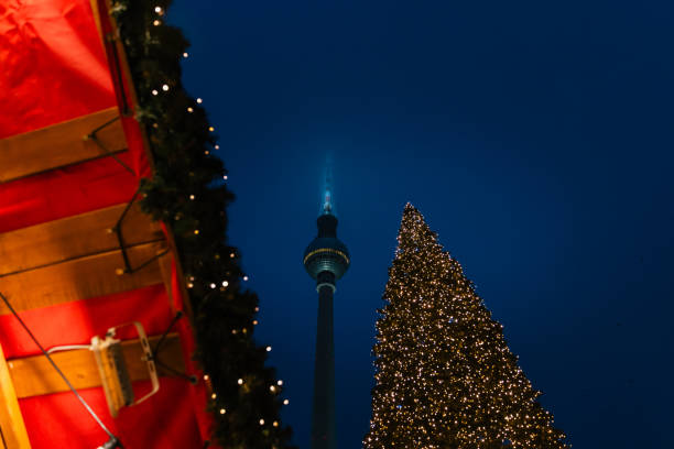 An enchanting view of the Berlin TV Tower illuminated against the dark night sky, with a beautifully decorated Christmas tree adorned with golden lights in the foreground. A perfect combination of modern architecture and festive charm