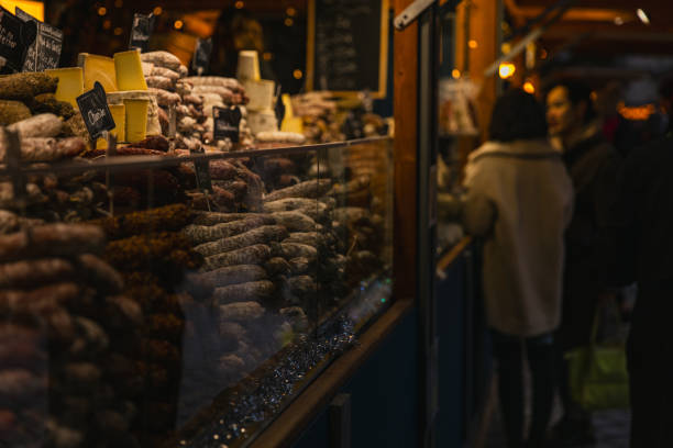 A detailed close-up of various cured and flavored sausages stacked in a festive market stall at the Berlin Christmas Market. The assortment showcases artisanal delicacies, including truffle-infused sausages, under warm lighting, creating a cozy holiday atmosphere
