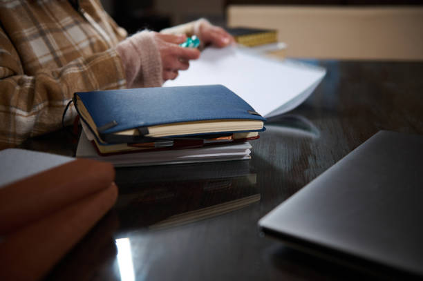 A person seated at a desk is seen writing in a notebook, with various stationery items, including a laptop, surrounding them. The environment is calm and organized, suitable for study or work.