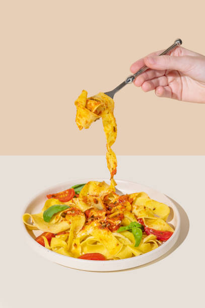 istock Hand holding fork with tagliatelle or pappardelle pasta with tomato sauce, basil and parmesan cheese in plate 2191036983