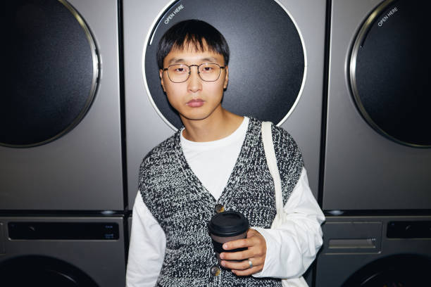 Portrait of modern Asian man with reusable cup in hand standing against washing machines