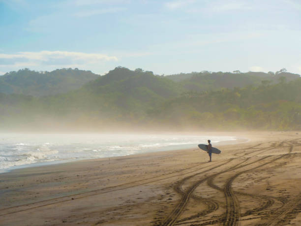 Surfer stands on a sandy shore before entering the water to ride some waves